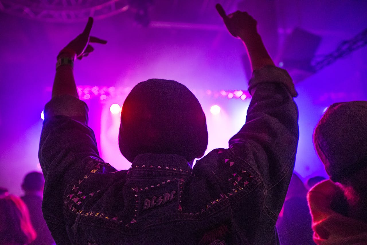Back view of a person enjoying an energetic nightclub scene with vibrant neon lights and music.