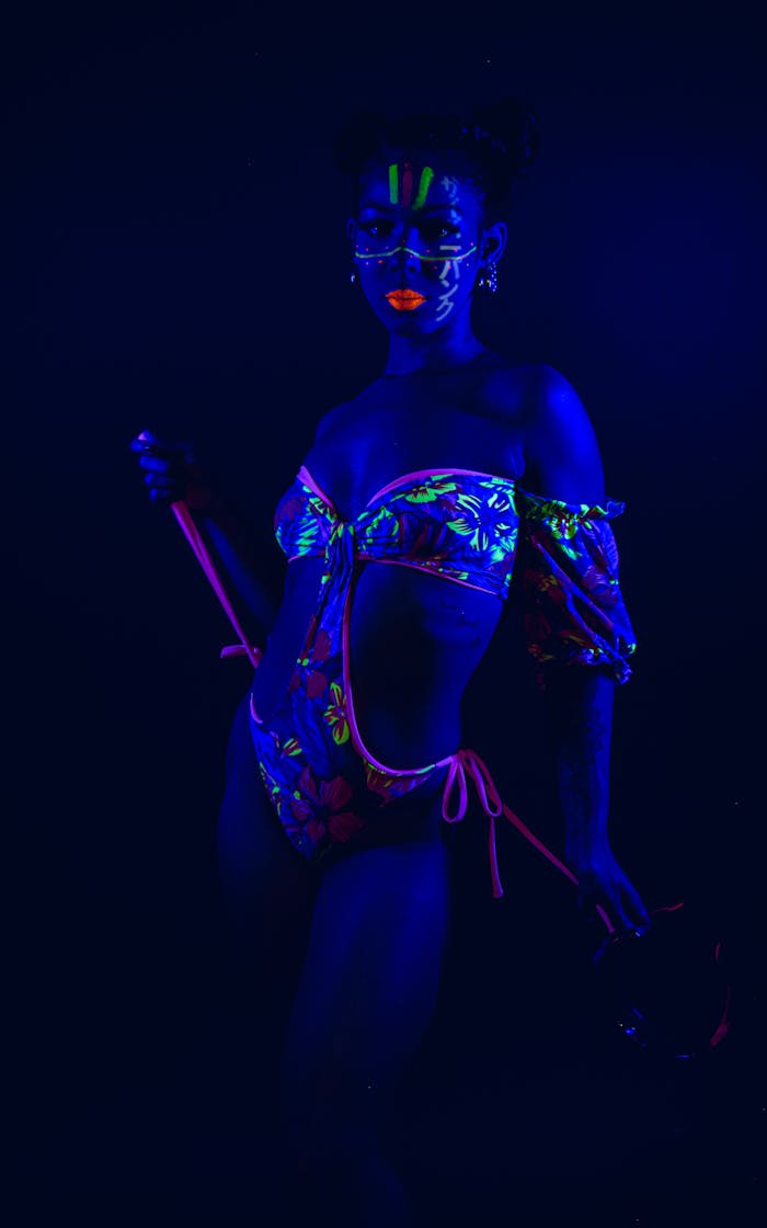 Artistic neon fashion portrait under blue UV light, showcasing bold makeup and colorful bikini.